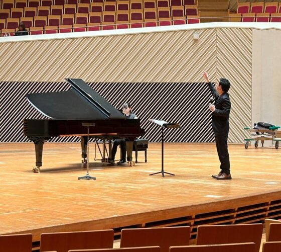 舞台上にはピアニストと指導をする指揮の中村さん。合唱はステージ後ろのP席で歌っている。