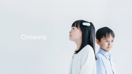 「オンテナ」ポスター画像。二人の子どもが、一人は髪に、もう一人はシャツの襟に白いバッジ型のオンテナをつけている。