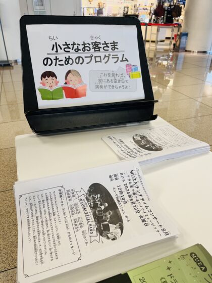 「小さなお客さまのためのプログラム」配布時の様子。子どものイラストが描かれた看板の前の机上に積み重ねられている。