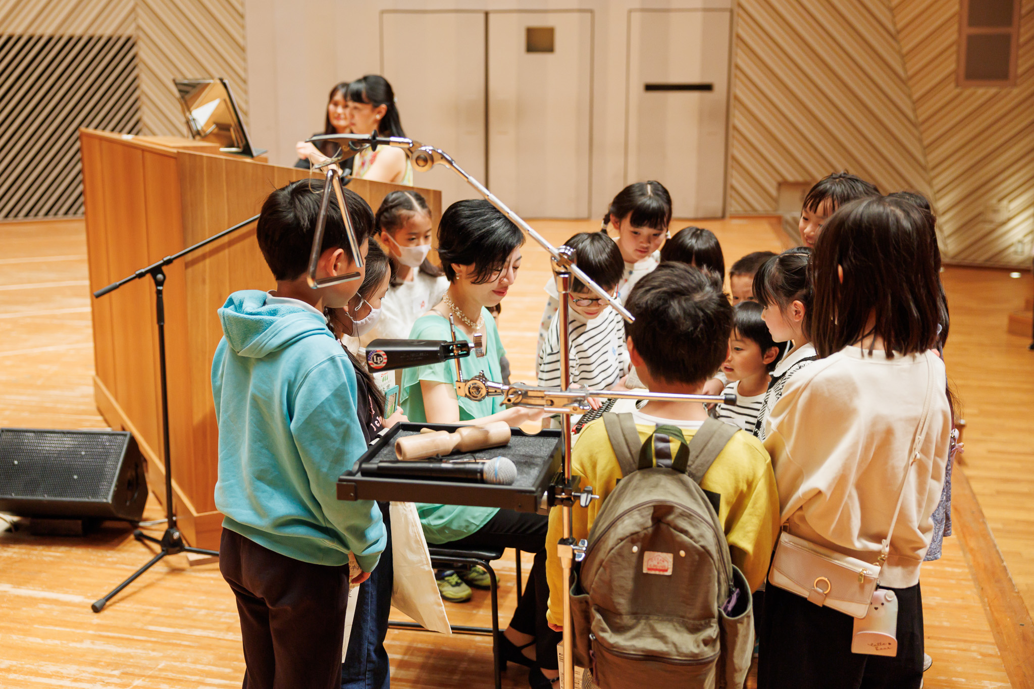 ステージ上で打楽器の牧野さんを子どもたちが囲って近くで音楽を楽しんでいる。奥で長田さんがオルガンを弾いている。
